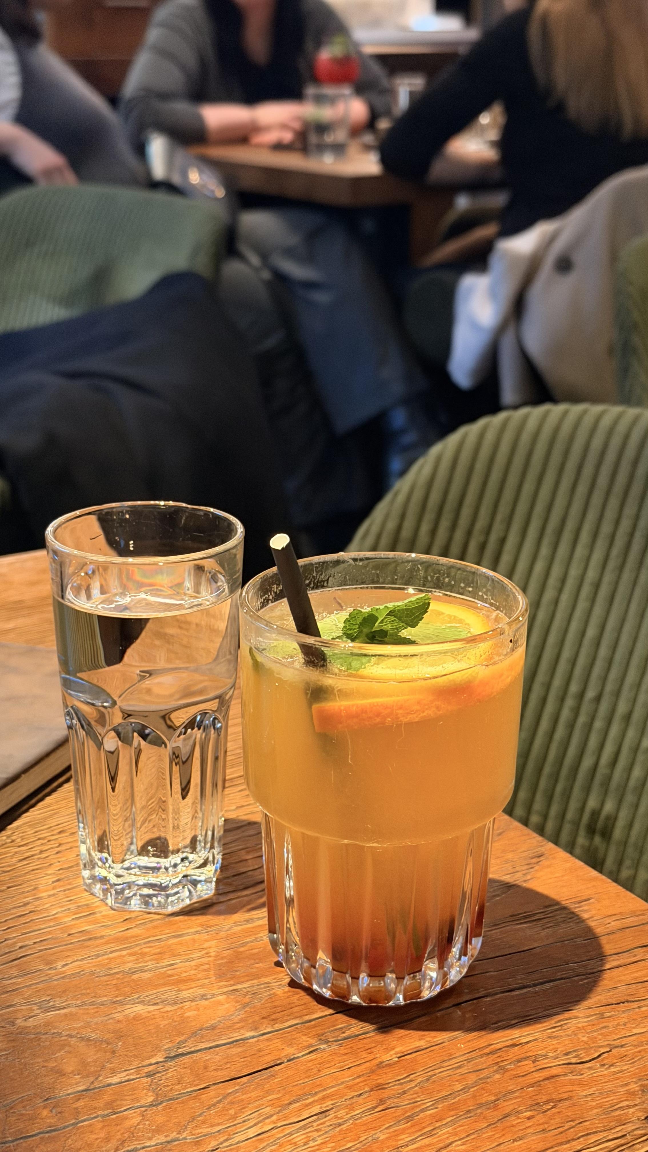 Pomarančni napitek z meto na leseni mizi v kavarni Mango